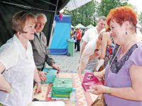 Kobieta w rudych włosach rozmawia ze sprzedawczynią przy zadaszonym straganie